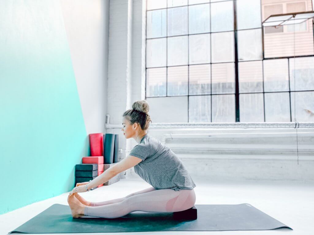 Woman using a yoga block under her hips for a Seated Forward Bend.