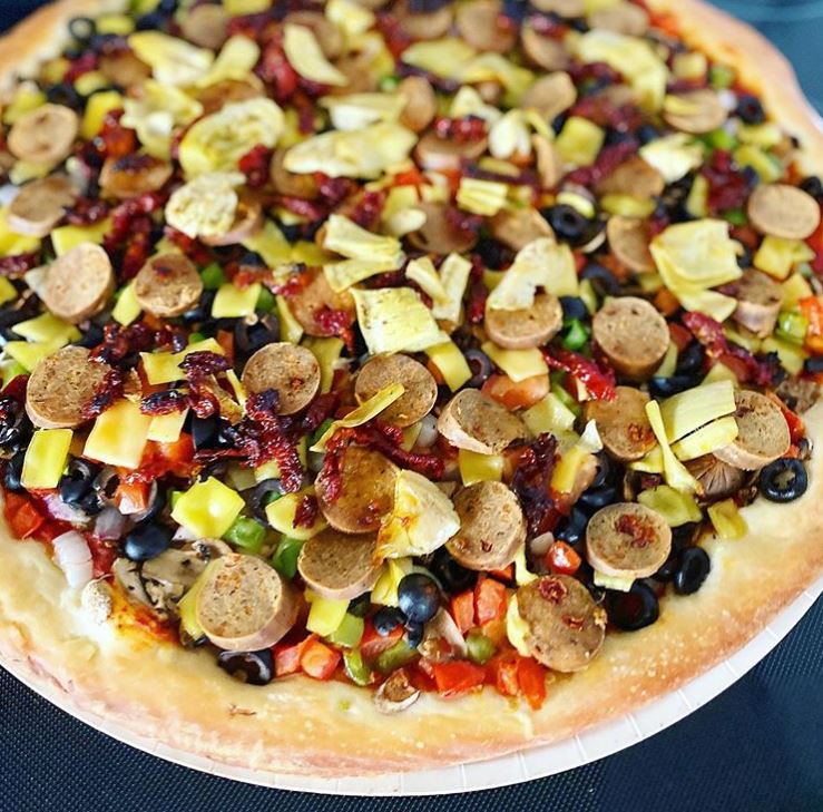 A delicious-looking pizza with vegan cheese and various toppings.